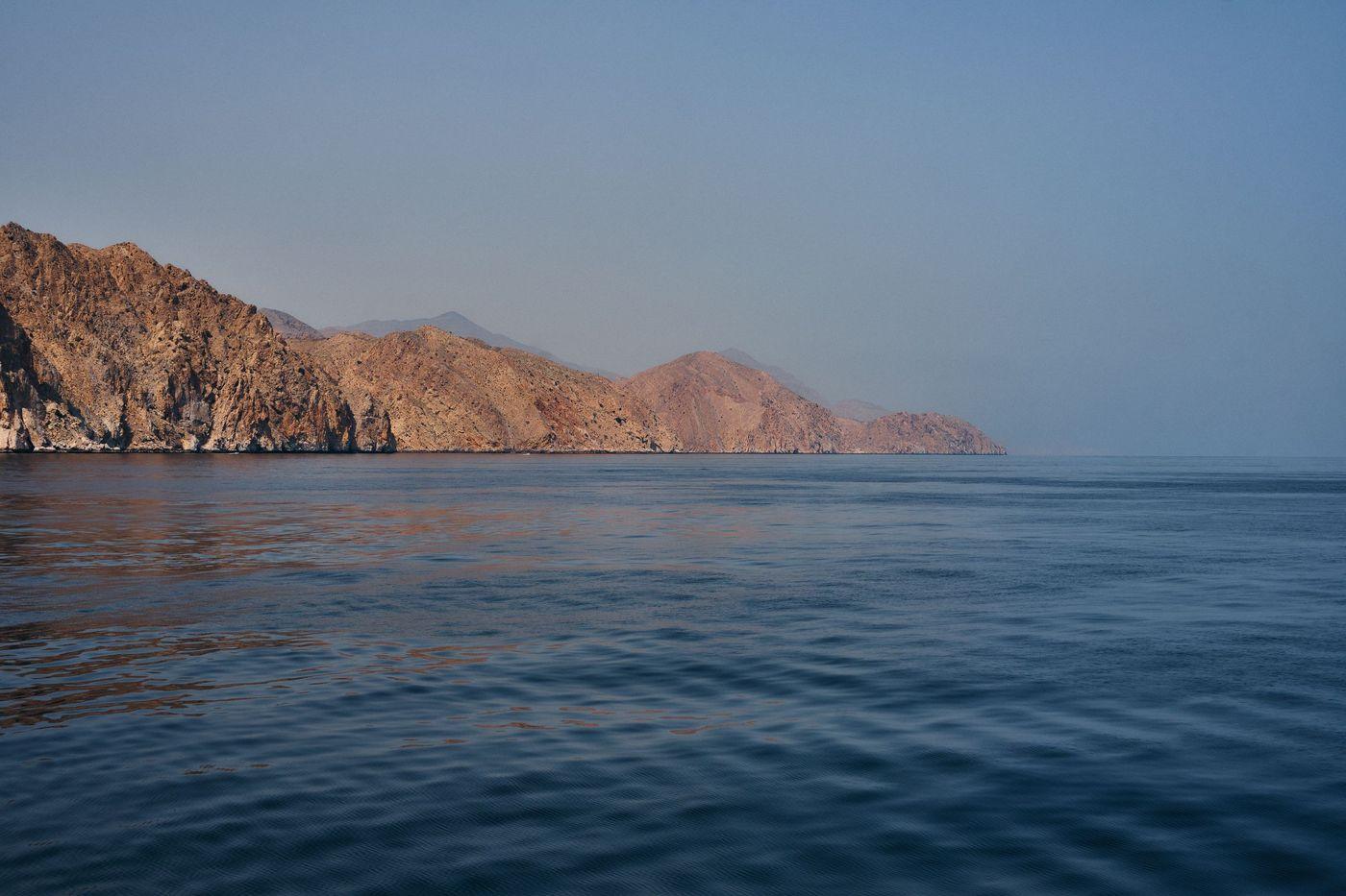 Arid rocky coastline meeting calm turquoise water in Oman